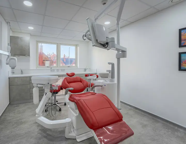 Consultorio dental luminoso con sillón rojo, lámpara y paredes blancas